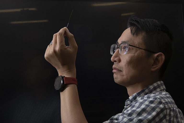 NASA electronics engineer Patrick Chan closely examines an optic fiber against a black background